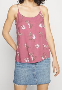 Różowa kwiatowa koszulka na ramiączkach z regulowanymi spaghetti. Zawiera motyle i małe kwiaty. Połączona z jasnoniebieską dżinsową spódnicą.