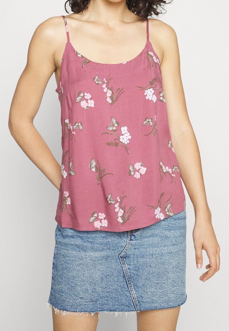 Różowa kwiatowa koszulka na ramiączkach z regulowanymi spaghetti. Zawiera motyle i małe kwiaty. Połączona z jasnoniebieską dżinsową spódnicą.