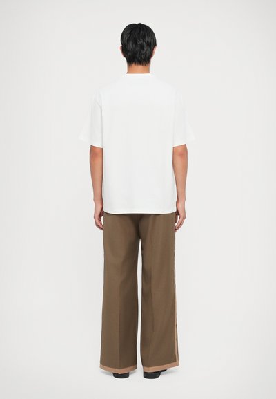 T-shirt bianco a maniche corte abbinato a pantaloni marroni a gamba larga con dettagli laterali e una vestibilità rilassata.