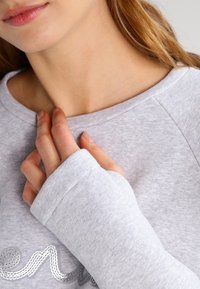 Sweat-shirt gris avec un encolure arrondie, des manches longues et une texture douce. Présente un détail en sequins formant un motif cursif sur la poitrine.
