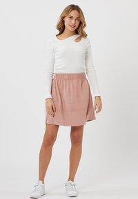 Maglietta bianca a maniche lunghe con uno scollo a goccia, abbinata a una gonna rosa lunghezza ginocchio con cintura elastica. Sneakers bianche.