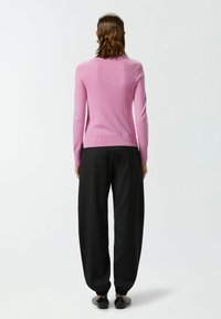 Maglione rosa a costine con un design aderente, maniche lunghe e scollatura rotonda, abbinato a pantaloni neri larghi e scarpe flat nere.