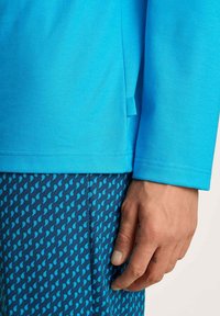 Felblau lange mouw shirt met een gladde textuur, gecombineerd met donkerblauwe korte broek met een patroon van lichtblauwe abstracte vormen.
