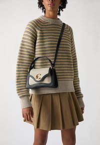 Sac à main structuré en cuir noir et toile beige, avec un fermoir doré. Pull en tricot rayé avec des tons neutres, associé à une jupe plissée kaki.