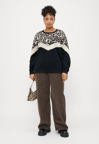 Juodas megztinis su gyvūnų raštais viršuje, smėlio spalvos zigzago detalė. Rudi aksominiai plačiakojai kelnių. Zebra rašto rankinė. Masyvūs juodi batai.