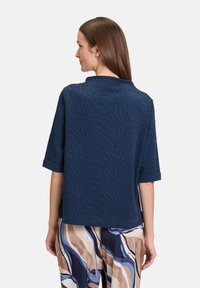 Granatowa, teksturowana bluzka z krótkimi rękawami i wysokim dekoltem. Materiał ma subtelny wzór, w zestawieniu z luźnymi spodniami w wzory.