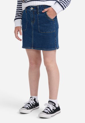 Saia de ganga em azul escuro, com bolsos frontais e costura laranja. Combinada com ténis pretos da Converse e meias brancas até ao tornozelo.