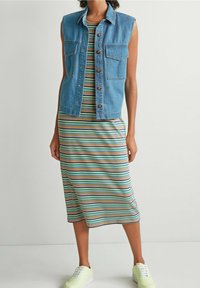 Gilet en denim sans manches, avec deux poches poitrine. Robe midi rayée dans des tons de bleu, vert et jaune. Baskets vert clair.
