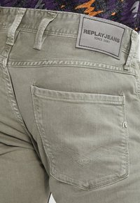 Jasnozielone dżinsy z denimu z tylną kieszenią, ozdobioną przeszytym wzorem i metką z napisem "REPLAYJEANS SINCE 1981".