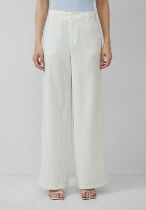 Witte wijde broek met subtiele lichtblauwe streepjes, met een vlakke voorkant, riemlussen en zijzakken. Gedragen met zilveren haksandalen.