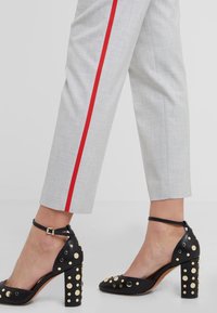 Pantalones grises de corte ajustado con una raya roja, combinados con tacones negros de tiras en el tobillo con tachuelas doradas y un tacón grueso.
