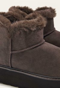 Braune Wildleder-Stiefeletten mit einem weichen Kunstfellkragen, flacher Sohle und einer gestickten Naht rund um die Basis.