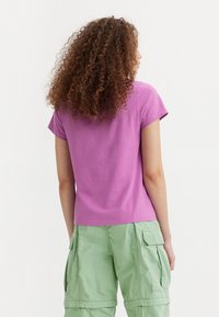 Lila kortärmad bomullströja med rundad halsringning, följsam textur och avslappnad passform, bärs tillsammans med ljusgröna cargobyxor.