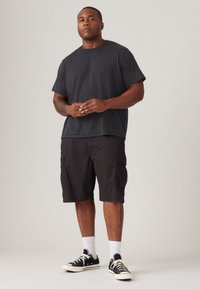 Svart kortermet t-skjorte med løs passform, kombinert med mørke cargo-shorts med sidelommer. Svart sneakers med hvite såler, hvite sokker.