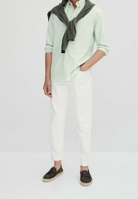 Lichtgroen gestreept shirt, grijze trui geknoopt om de nek, witte broek en donkerbruine loafers met gevlochten zolen. Casual zomerkleding.