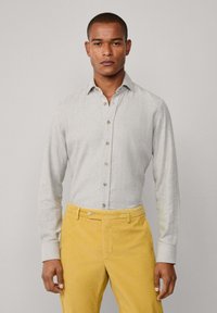 Camisa de manga larga de color gris claro con cuello abotonado y botones marrones, combinada con pantalones amarillos mostaza, que presentan una textura suave.