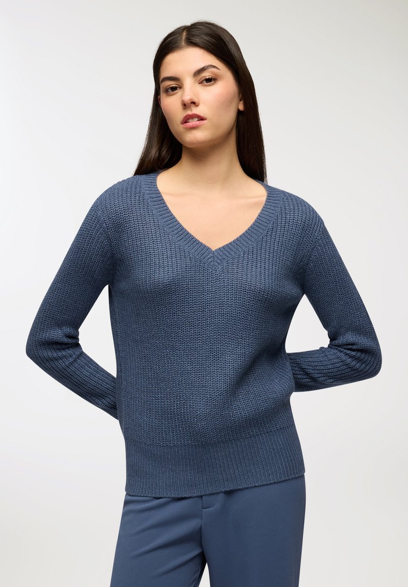 Sweter dzianinowy w serek w ciemnoniebieskim kolorze, z prążkowanymi mankietami i dołem. Materiał ma teksturowany wzór, zestawiony z pasującymi niebieskimi spodniami.