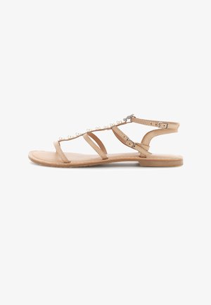 Sandalia plana beige con múltiples tiras finas, adornos de perlas a lo largo de la tira superior y cierres de hebilla en el tobillo.