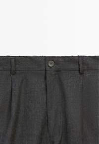 Tmavě šedé plisované kalhoty s strukturovanou tkaninou, zapínáním na knoflík a poutky na opasek. Design je střižen tak, aby vytvářel přiléhavý profil.