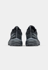 Paire de chaussures de trail Salomon noires et grises vues de dos, avec des semelles épaisses et des languettes aux talons.