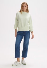 Felpa verde chiaro a coste con scollo ampio e maniche a tre quarti, abbinata a jeans blu a vita alta e sneaker bianche.