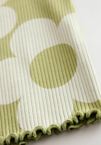 Grüner und weißer gerippter Stoff mit großen, kreisförmigen Mustern und einem welligen Saum am unteren Rand für zusätzliche Textur.