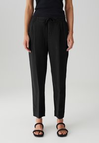 Pantalons noirs légers avec une taille élastique et un cordon de serrage ajustable, présentant une jambe fuselée et des plis à l'avant.