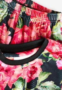 Blommönstrad tyg med stora rosa rosor på en mörk bakgrund. Svart kant vid halsen; elastisk midja på den tillhörande delen.