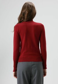 Rode trui met lange mouwen en hoge hals, aansluitend model, geribbelde manchetten en een gladde textuur, gecombineerd met grijze broek.