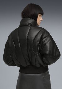 Zwarte pufferjack met een hoge kraag, met een glanzende textuur, oversized proporties en ribgebreide zwarte manchetten bij de taille.