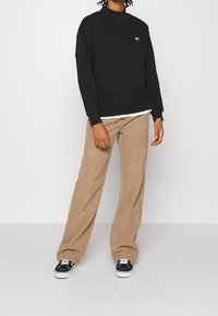 Sudadera negra de cuello redondo con un pequeño logo, combinada con pantalones de sarga anchos de color beige y zapatillas negras con suelas blancas.