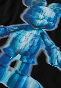 Mėlyno atspalvio, pikselizuota Mikio Peleko figūra su šypsena juodame fone, su skaitmeniniu gedimu per visą kūną.