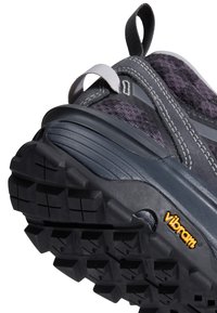 Gros plan sur la semelle d'une chaussure de randonnée noire et gris foncé avec des crampons profonds et un logo Vibram jaune sur le côté.