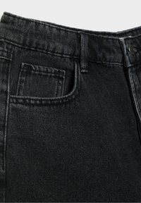 Gros plan sur la taille d'un jean en denim noir montrant la passants de ceinture, la poche avant, la petite poche à monnaie et la fermeture par bouton métallique.