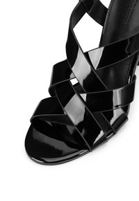Spīdīgas melnas patentētas ādas augstpapēžu sandales ar šķērsām siksniņām un atvērtu purngalu. Gluda tekstūra un eleganta siluete.