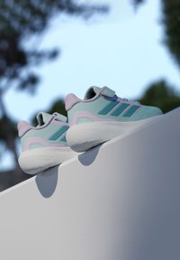 Αθλητικά παπούτσια ανοιχτού μπλε με ροζ λεπτομέρειες, υφασμάτινη επάνω επιφάνεια με υφή, και τρεις τυρκουάζ ρίγες. Περιλαμβάνουν λουράκι με βέλκρο και μαλακή σόλα από αφρό σύννεφο.