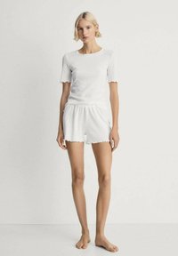 Top corto bianco in cotone a maniche corte con texture a coste e maniche scallop, abbinato a pantaloni corti con orlo scallop simile.