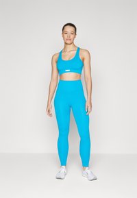 Blå treningssett bestående av en crop top med brede stropper og høyt liv leggings i ribbet tekstur. Fullført med hvite joggesko.