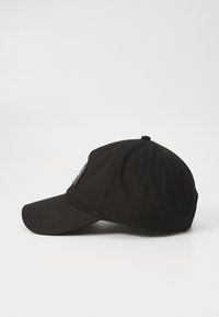 Zwarte baseballpet met een gebogen rand, gemaakt van katoen. Beschikt over een gestructureerde zwarte patch aan de zijkant en stiksels op de rand.