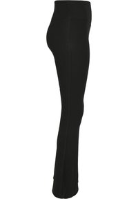 Pantalon de yoga noir taille haute avec une silhouette ajustée, montré de profil sur fond blanc.