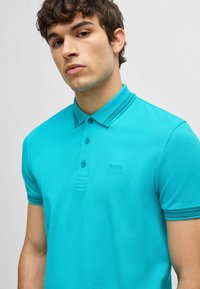 Turkos polo skjorta i texturerad tyg, med krage, tre-knapp placket och broderad logotyp. Kontraststripes på kragen.