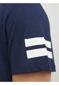 Camiseta de algodón azul marino con rayas horizontales blancas en las mangas. Textura suave, diseño de cuello redondo y mangas cortas.