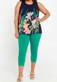 Blommönstrad ärmlös topp i marinblått med gröna detaljer; matchad med åtsittande gröna capribyxor och sandaler med remmar i vitt.