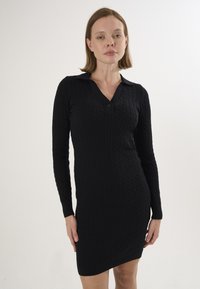 Robe en tricot noir à manches longues, avec un motif de câble côtelé, un col en V et une fermeture à bouton au cou.