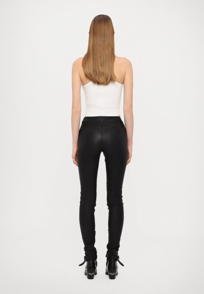 Černé skinny kalhoty vyrobené z hladkého materiálu, design s vysokým pasem, spárované s bílým upnutým topem a černými kotníkovými botami se straps.
