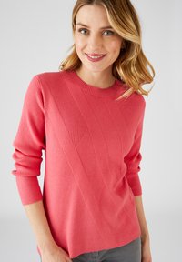 Maglione rosa a coste con un motivo diagonale testurizzato, collo rotondo e maniche lunghe. Il materiale sembra morbido e lavorato a maglia.