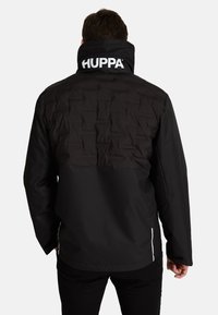 Melna jaka arpuse ar polsterētu augšējo daļu, augstu apkakli ar "HUPPA" logotipu. Materiāls izskatās gluds, ar brīvu piegriezumu un garām piedurknēm.