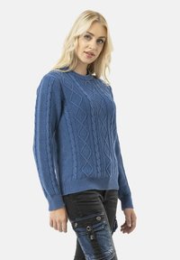 Pull en tricot bleu avec un motif texturé, encolure et poignets côtelés. Porté avec un jean de couleur foncée mettant en valeur des accents de poches.
