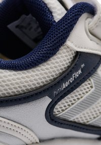 Witte sportschoen met marineblauwe accenten, voorzien van een bovenwerk van mesh, gestructureerde synthetische overlays en zichtbare merklogo's aan de zijkant.