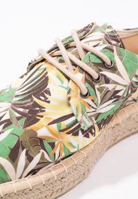 Šněrovací boty s tropickým květinovým vzorem v zelené, žluté a hnědé barvě. Jutová mezi podrážka dodává texturu a přírodní detail.